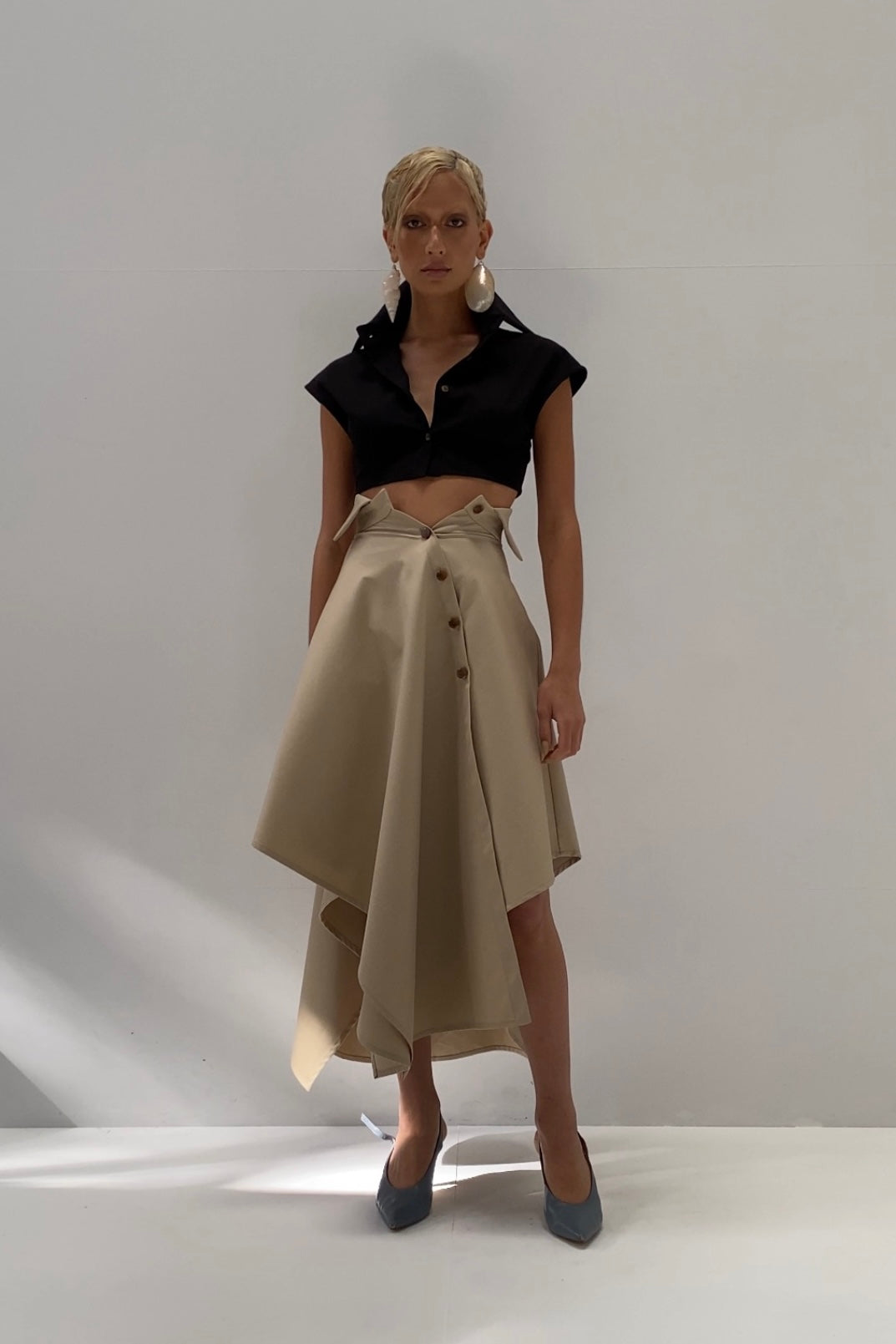Woman in black cropped sleeveless button up shirt. Styled with beige skirt.