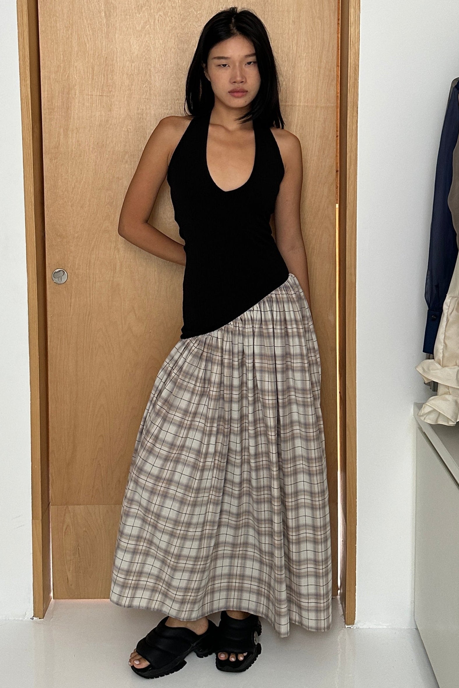 Woman in a black halter maxi dress with v-neck line and asymmetric artfully gathered plaid skirt. Top flatters the figure and skirt adds flow with every movement. Perfect for beach outings and summer soirées.