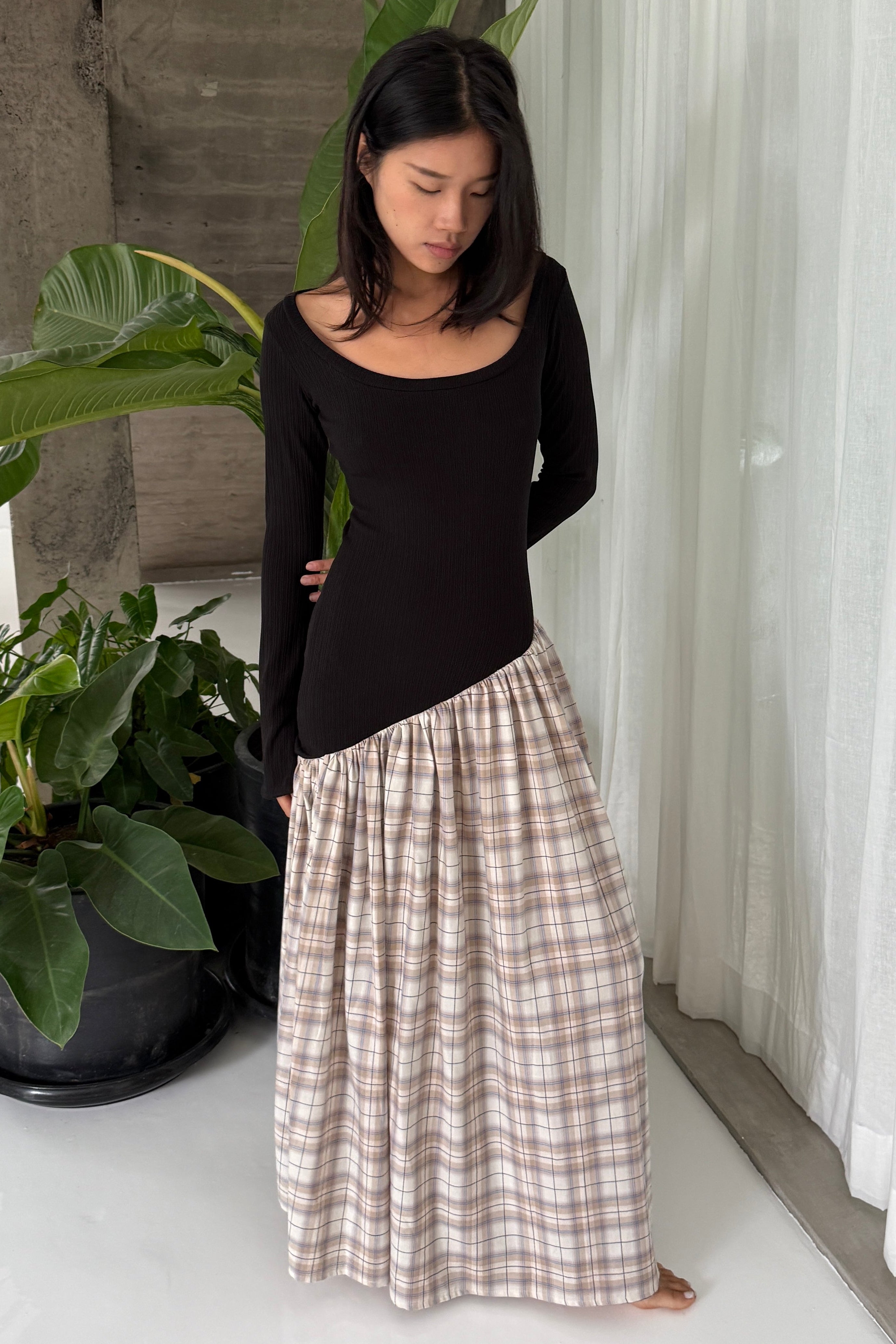 Woman in black maxi dress, with extra long sleeves, scooped neckline, and artfully gathered plaid skirt. Top flatters the figure whilst the skirt flows with every movement. Can be dressed up or down.