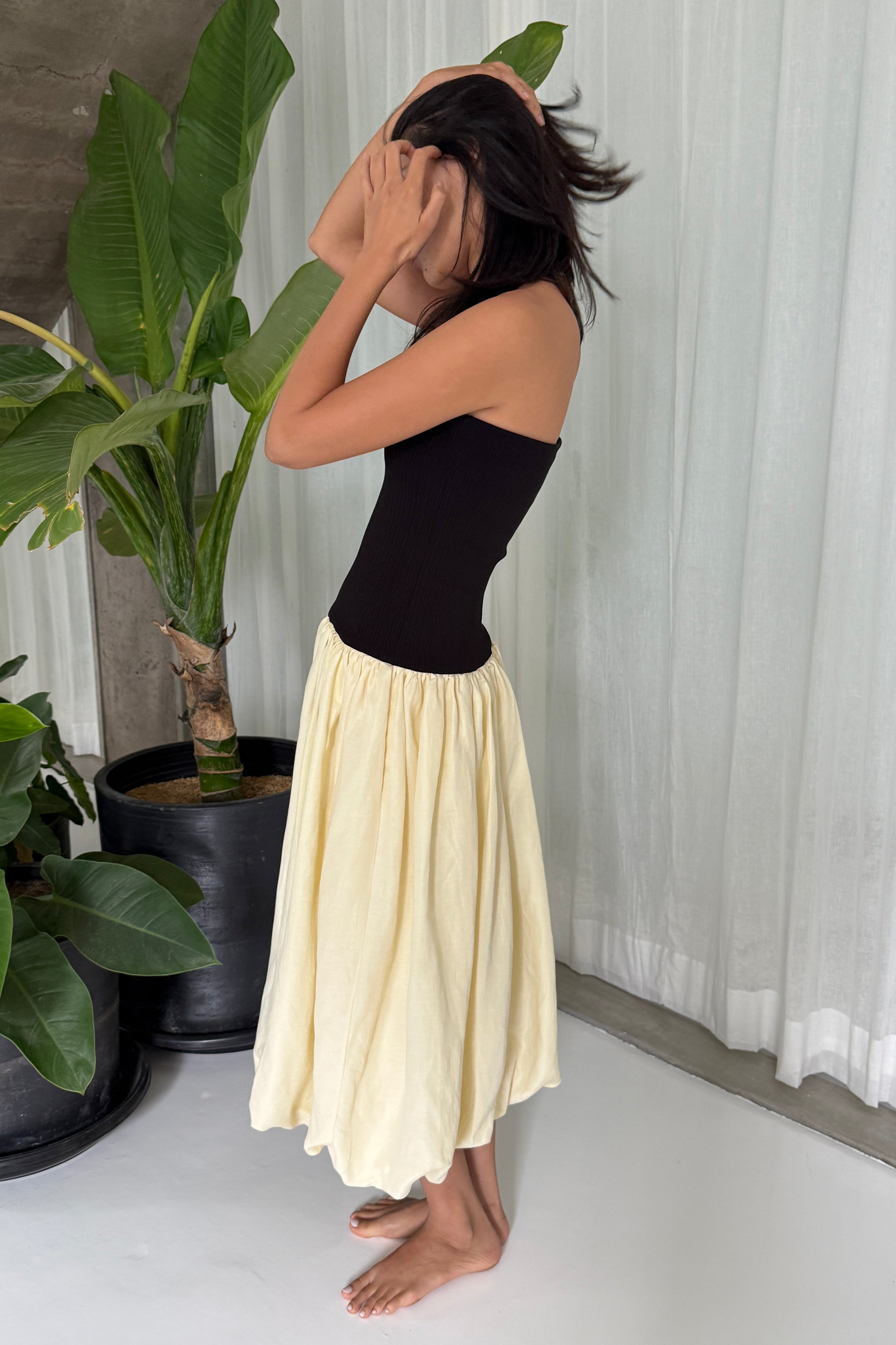 Woman in strapless black midi dress with artfully gathered lemon balloon skirt. Perfect for Summer soirées.