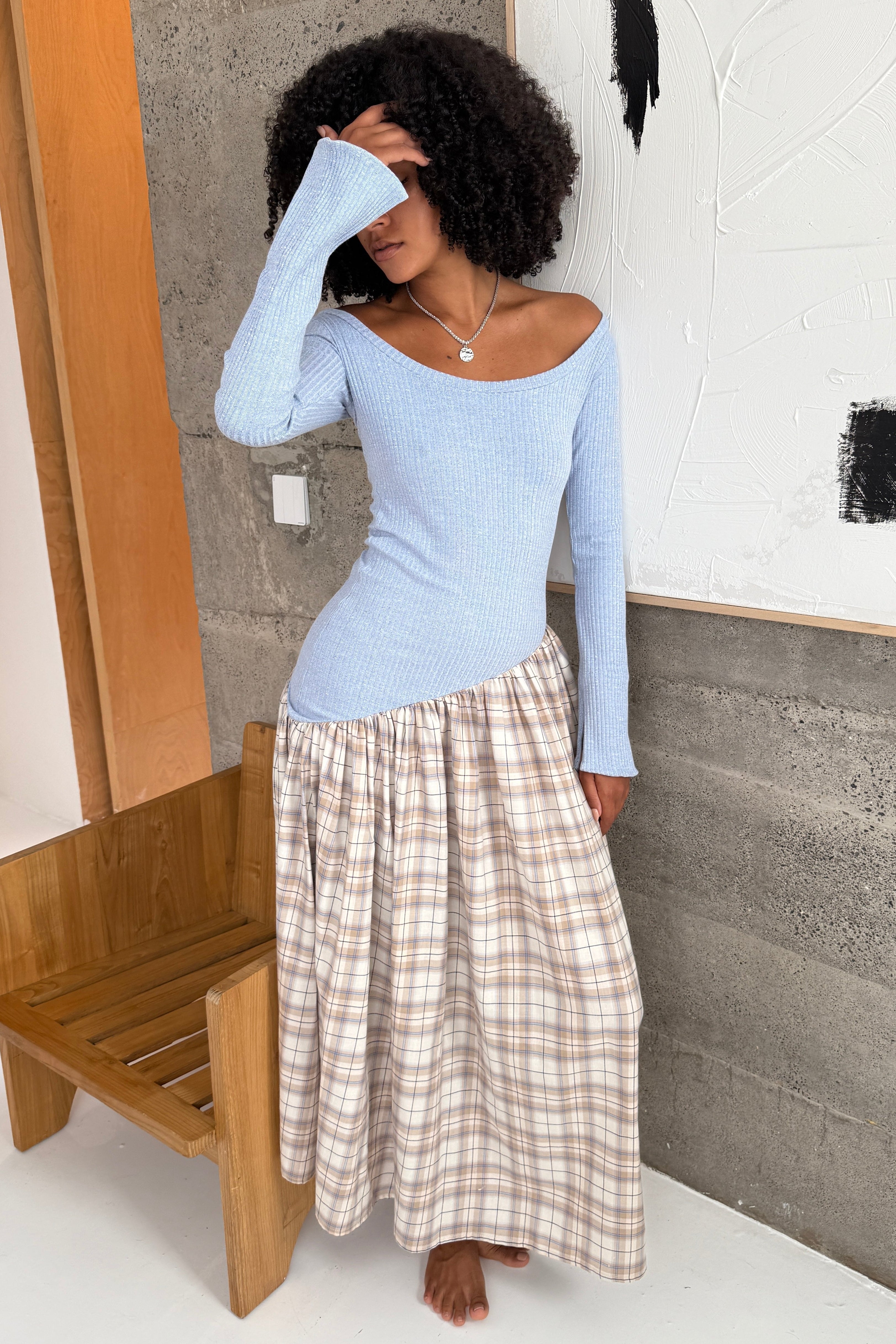 Woman in long sleeve dress, with extra long sleeves, scooped neckline, and artfully gathered asymmetric plaid skirt. Top flatters the figure whilst the skirt flows with every movement. Can be dressed up or down. Styled with silver necklace.