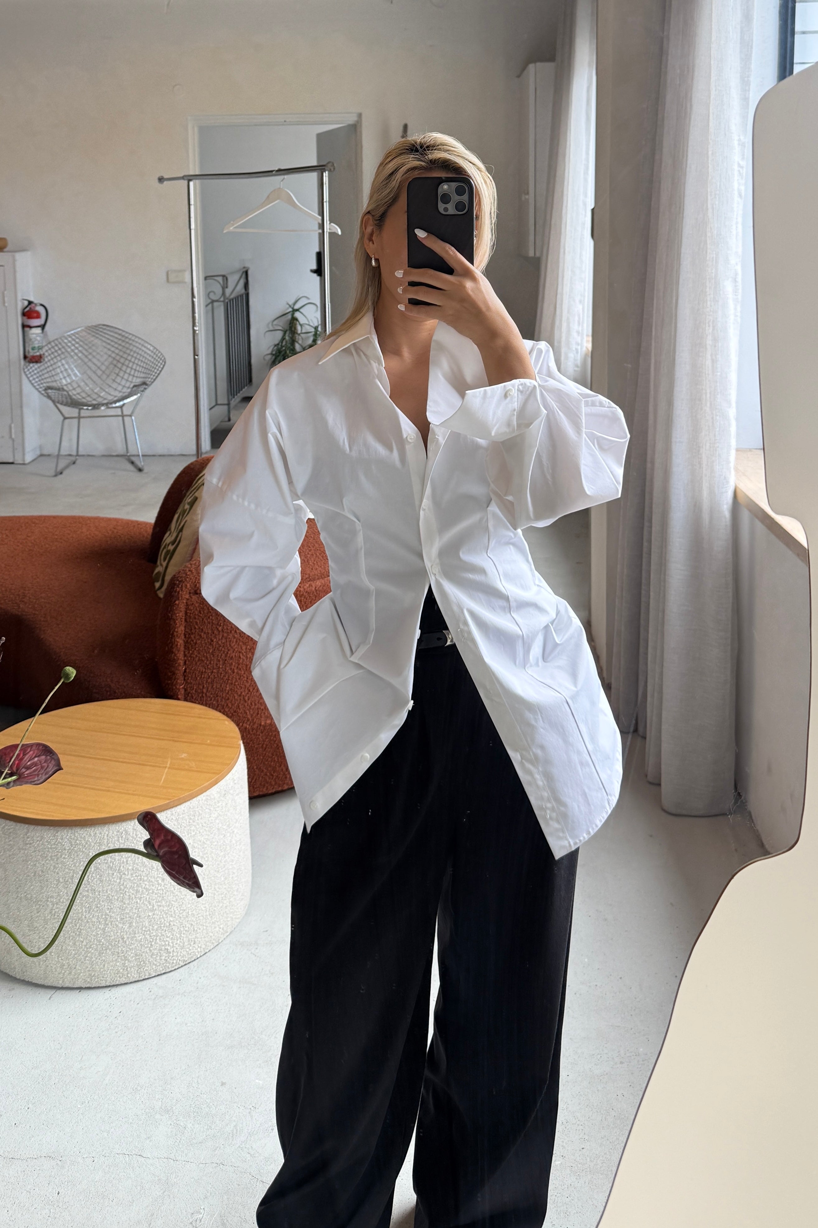 Woman in white volume sleeve shirt dress. Slightly unbuttoned and styled over black trousers.