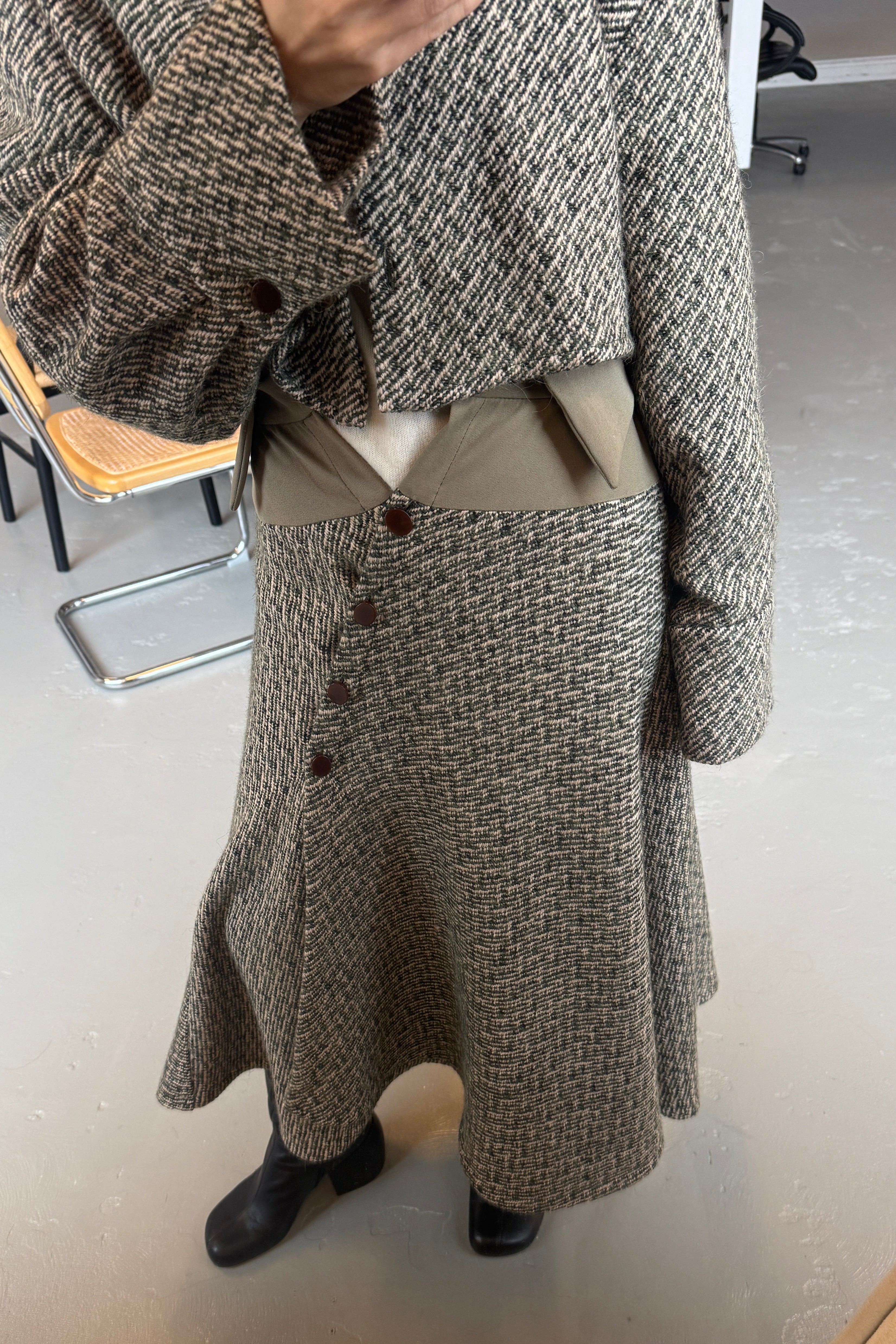 Woman in olive Japanese wool bouclé midi handkerchief hem skirt with button front closure. Styled with matching jacket.