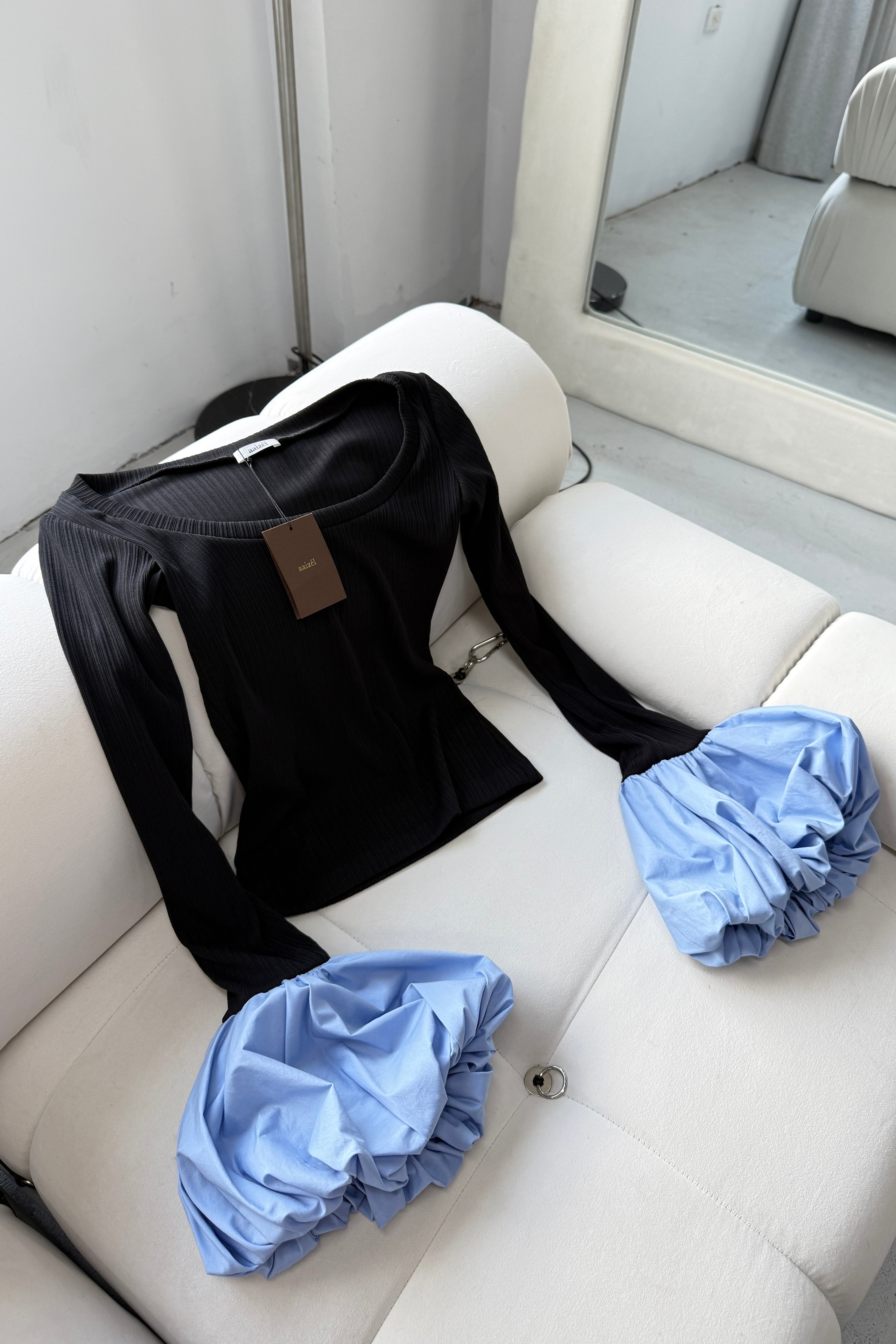 Flat lay of black long sleeve rib knit top with round neckline and blue balloon details on cuffs. 