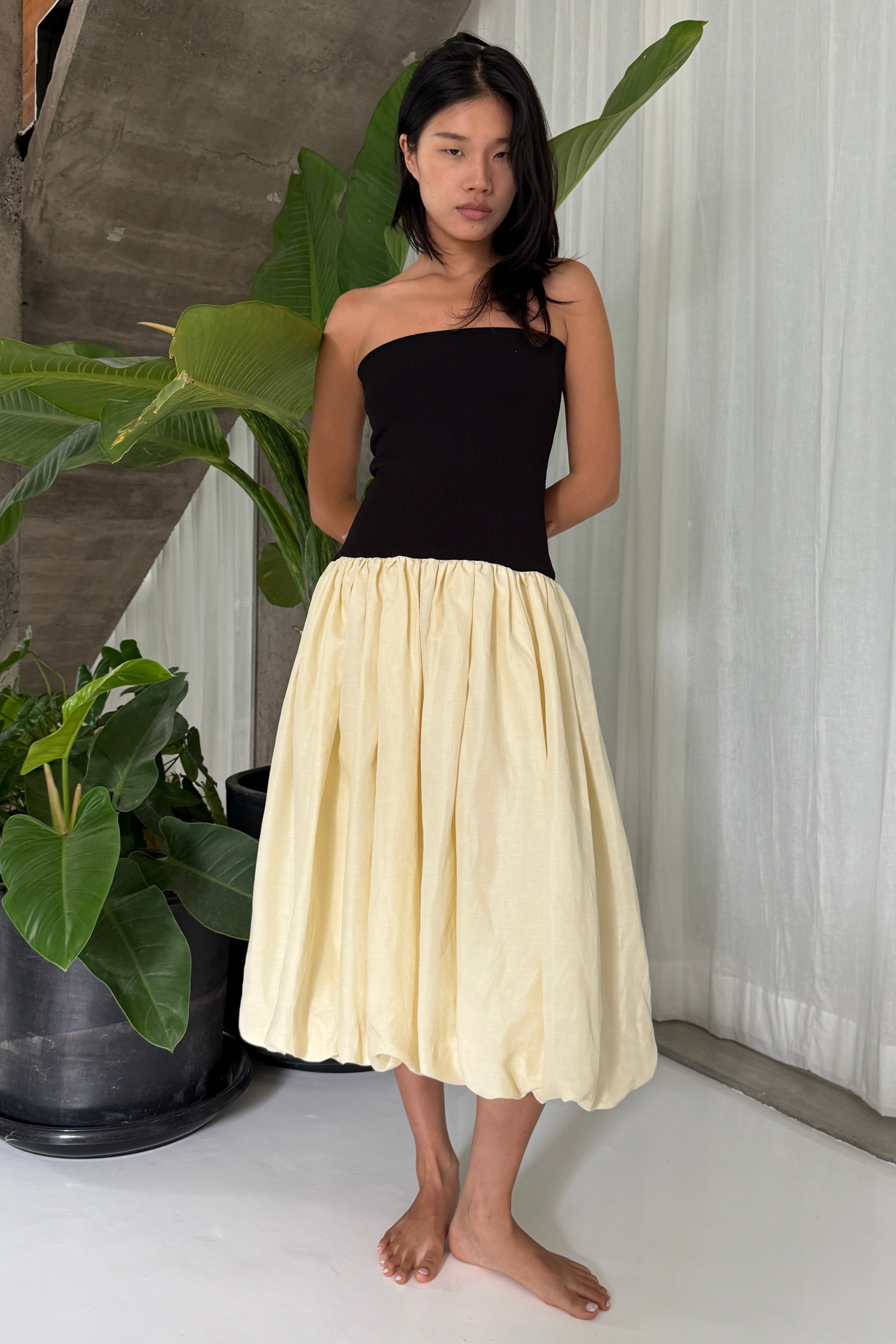 Woman in strapless black midi dress with artfully gathered lemon balloon skirt. Perfect for Summer soirées.
