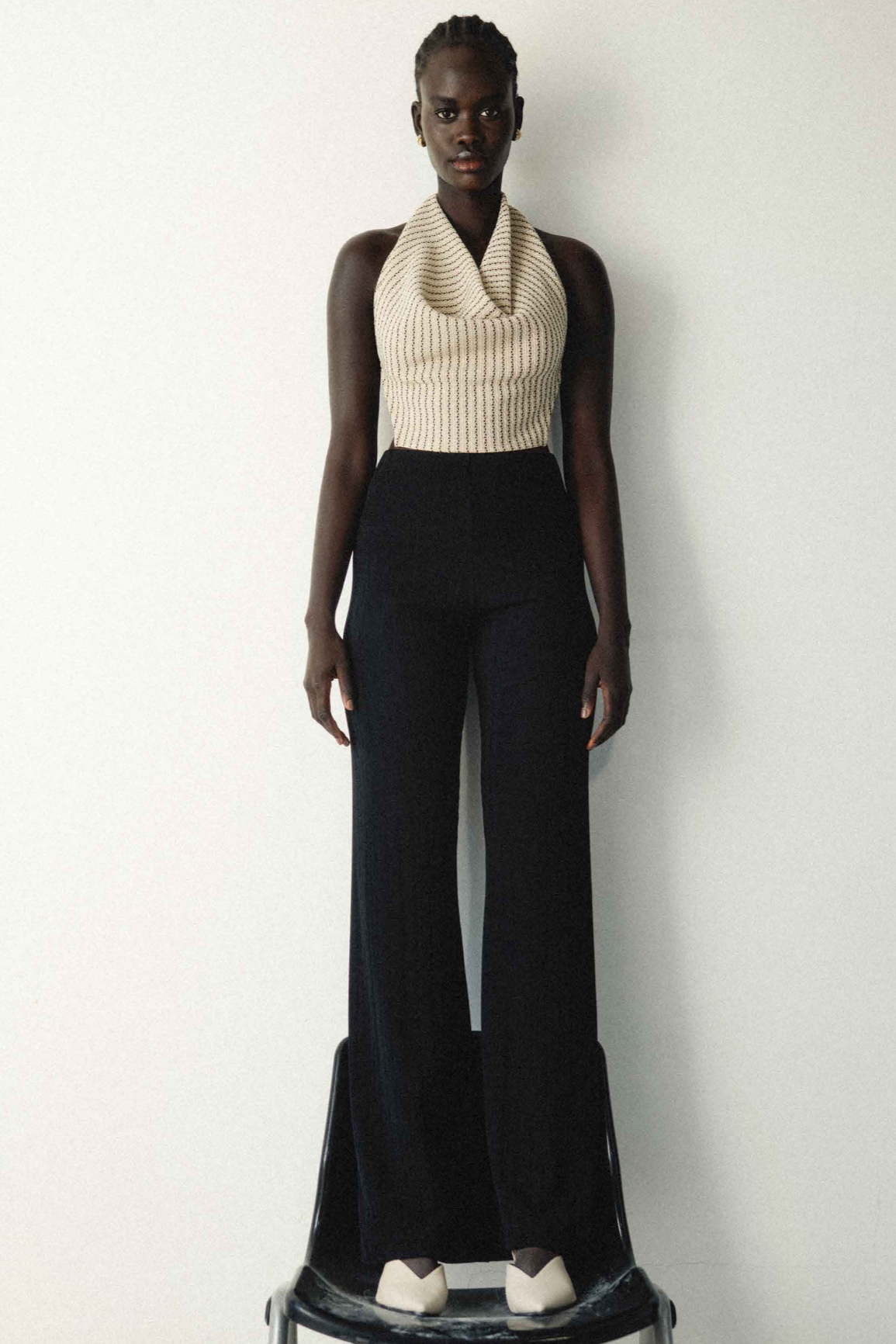 Woman in cropped black beige white striped cowl neck top with tie back. Paired with black wide leg pants.