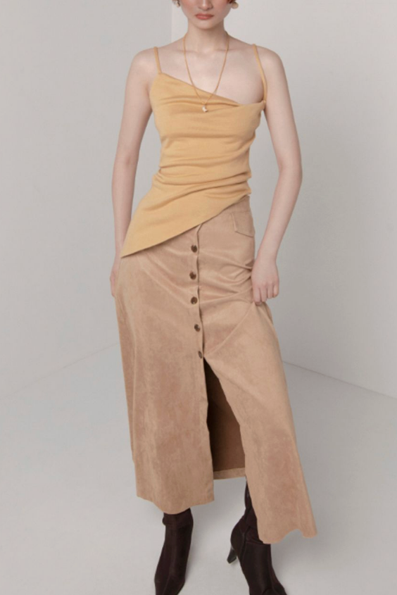 Woman in custard cowl neck asymmetric hem top. Styled with brown buttoned maxi skirt.